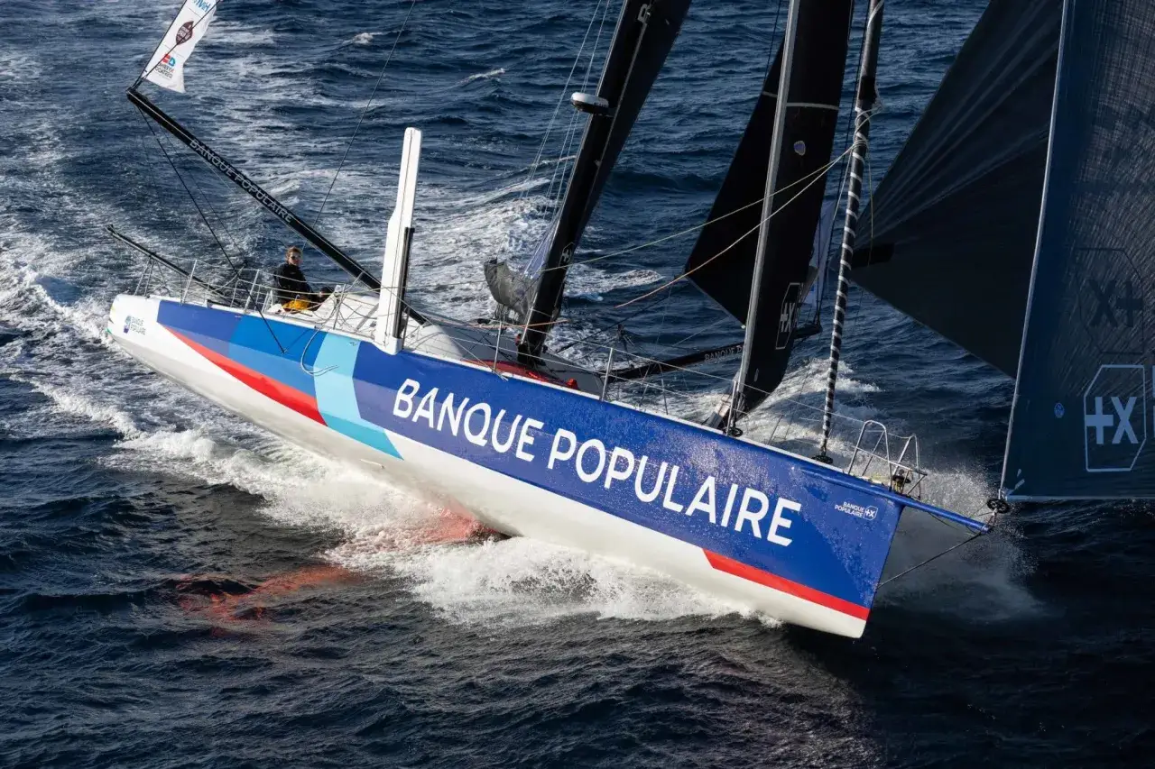 Clarisse Crémer navigue sur le voilier Banque Populaire, fendant les vagues bleues avec détermination.