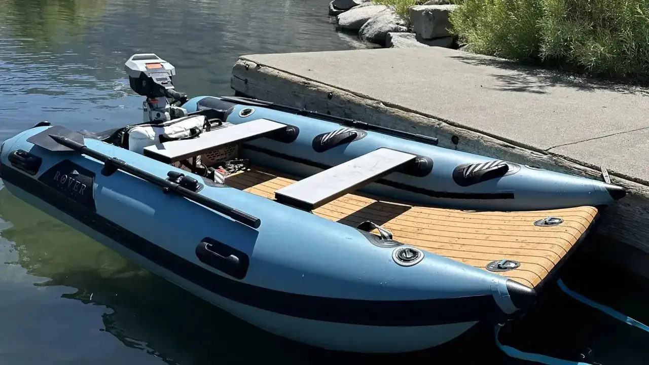 Une petite barque bleue, prête à rejoindre son bateau, est amarrée à un ponton en bois. Elle est équipée d'un moteur hors-bord et de rames.