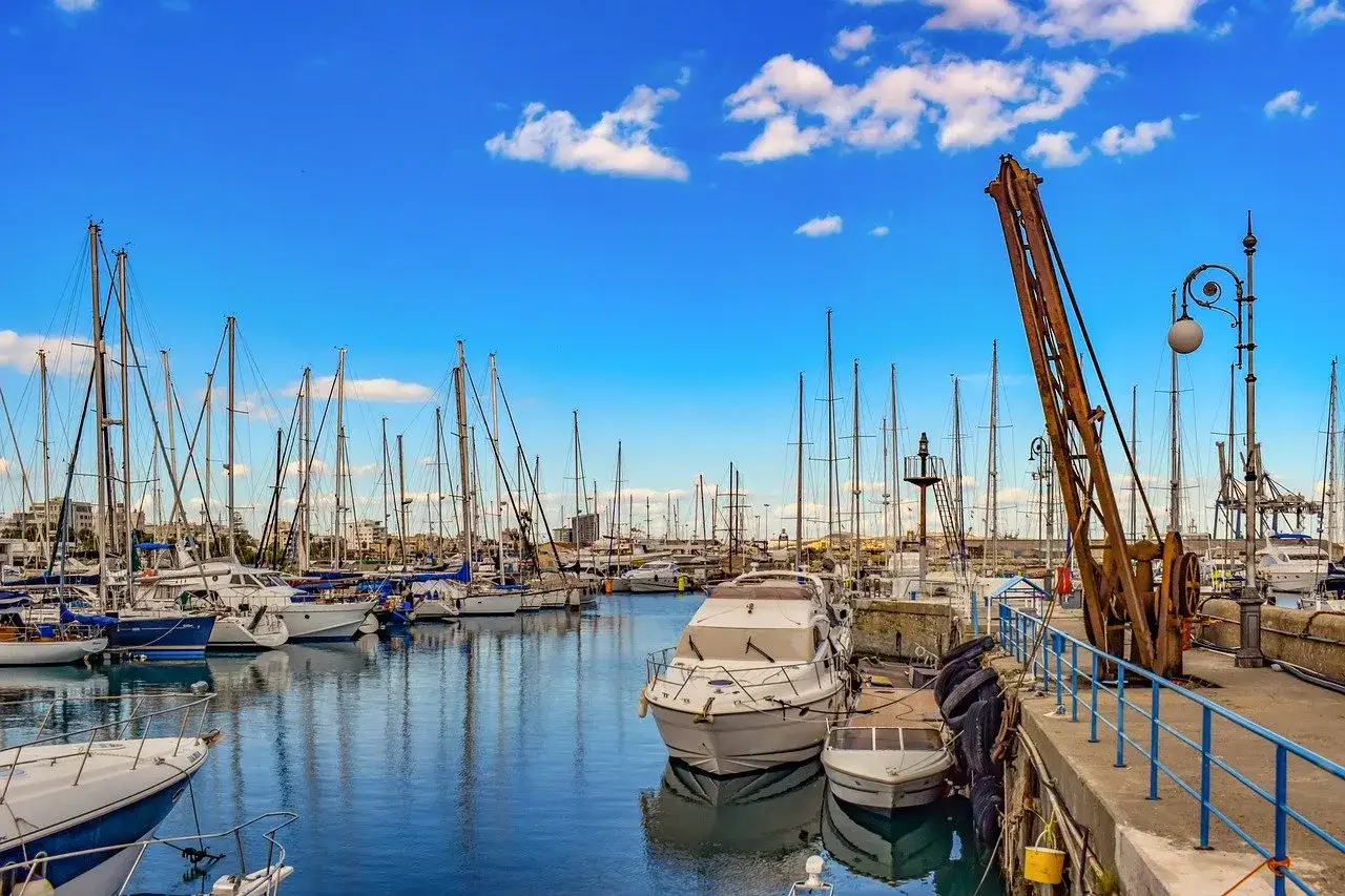 Port animé avec voiliers et bateaux à moteur. Un vieux portique rouillé se dresse sur la droite. Idéal pour estimer le prix entretien bateau.