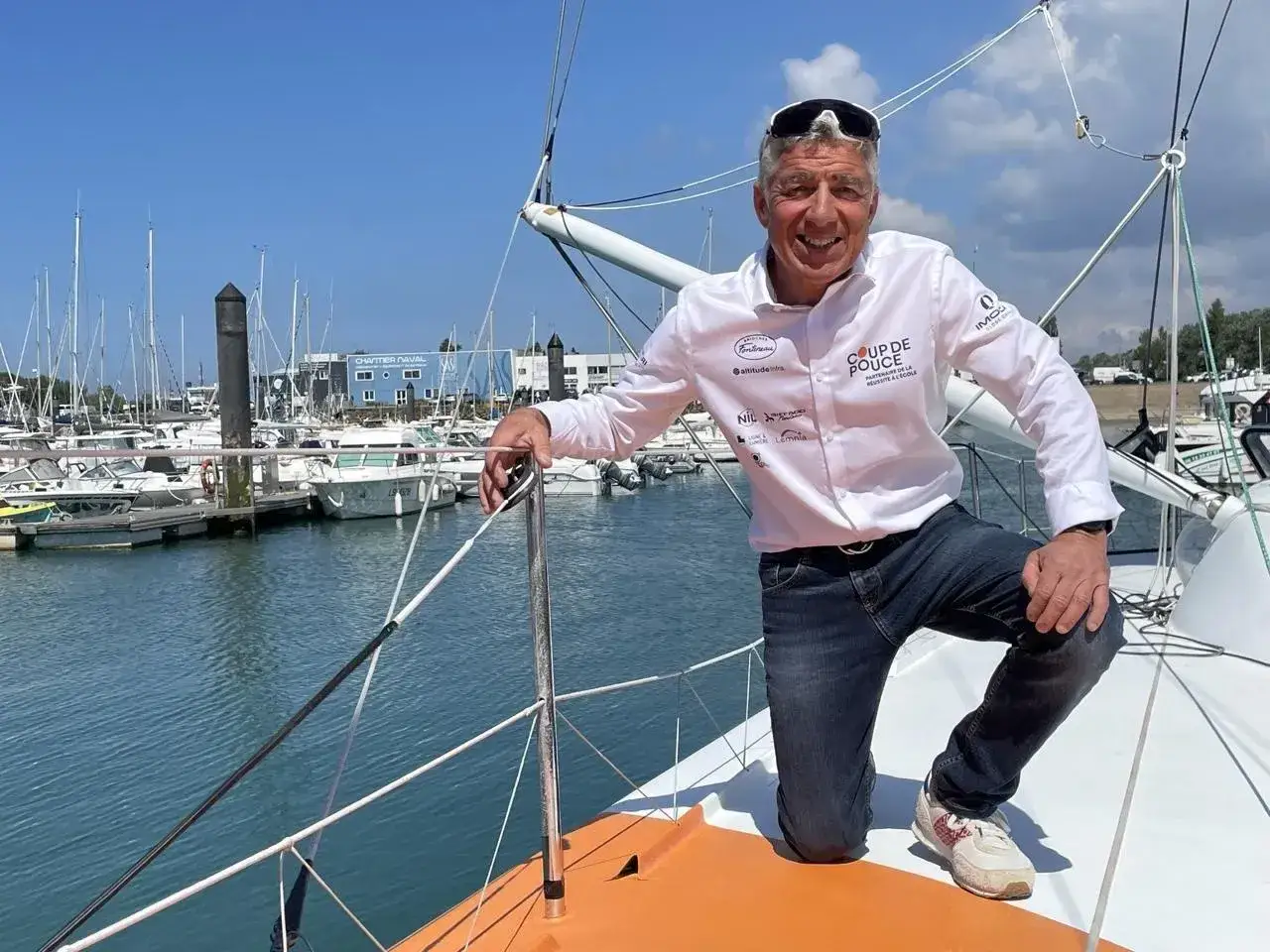 Manuel Cousin, skipper souriant, pose sur son voilier dans un port de plaisance.