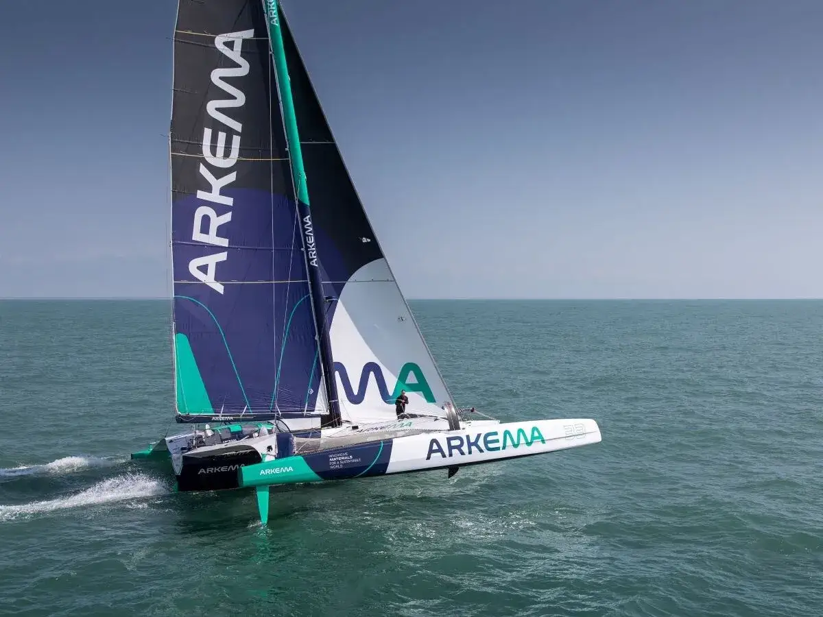 Trimaran Arkema 53 fend l'océan, ses voiles portant le nom de son sponsor. Un spectacle de vitesse et de technologie sur l'eau.