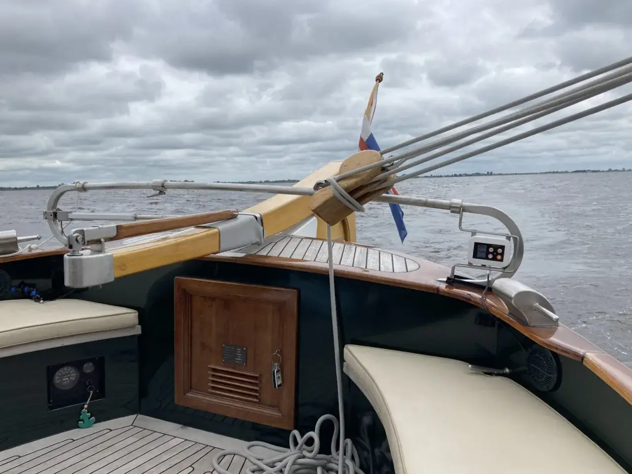 Vue arrière d'un bateau avec barre franche en bois, drapeau néerlandais et cordages. Le ciel est couvert.