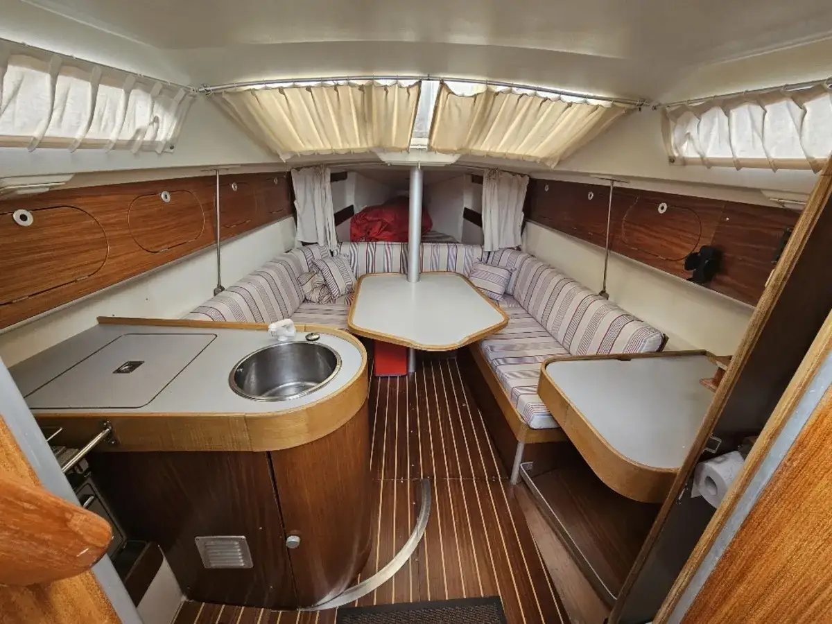 Intérieur du bateau, étape 28 : coin cuisine avec évier, banquettes rayées et tables. Ambiance chaleureuse et boisée.