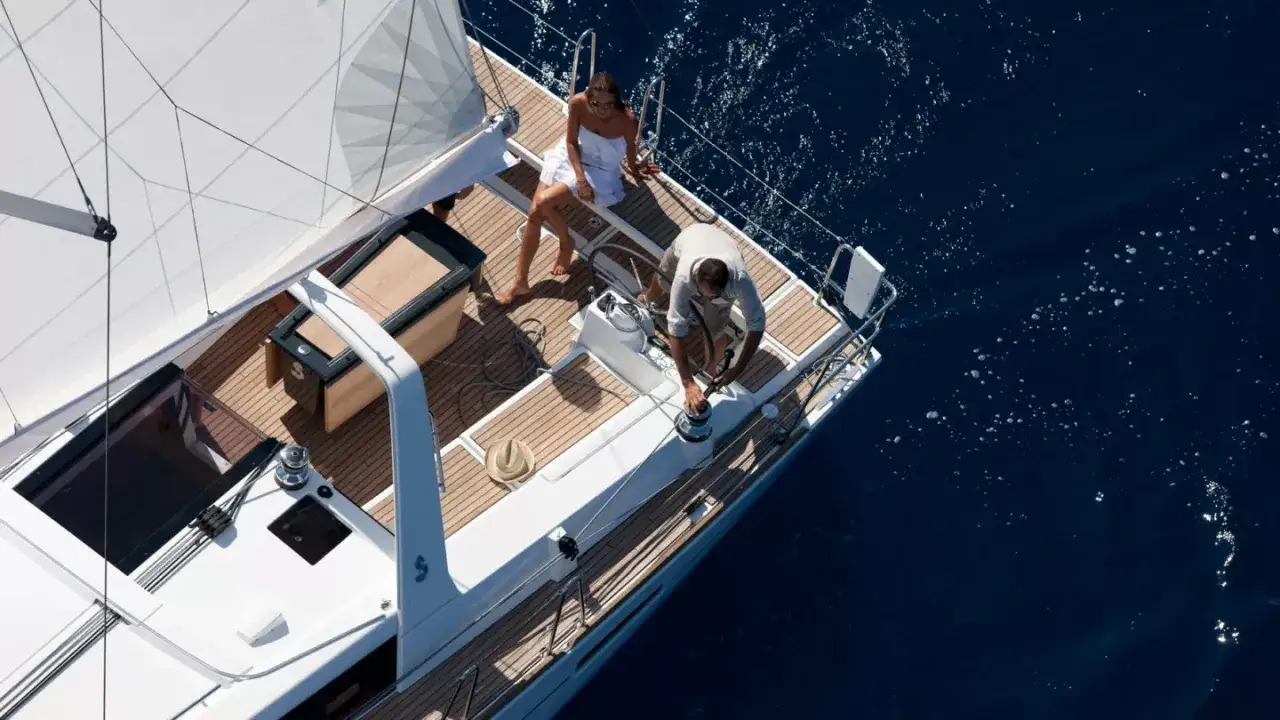 Un couple profite d'une croisière sur un voilier, comme le montre la fiche technique de l'Oceanis 45. L'homme manœuvre le winch, la femme se repose.
