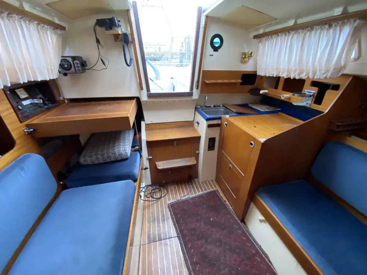 Intérieur du Dufour 2800 : banquettes bleues, table escamotable, évier, et tapis. Prêt pour l'aventure !