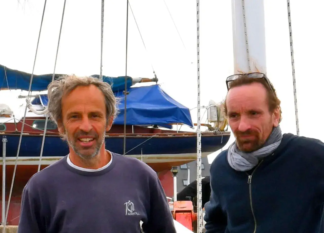 Nicole Van de Kerckhove et un ami sur un voilier, prêts pour une aventure maritime.