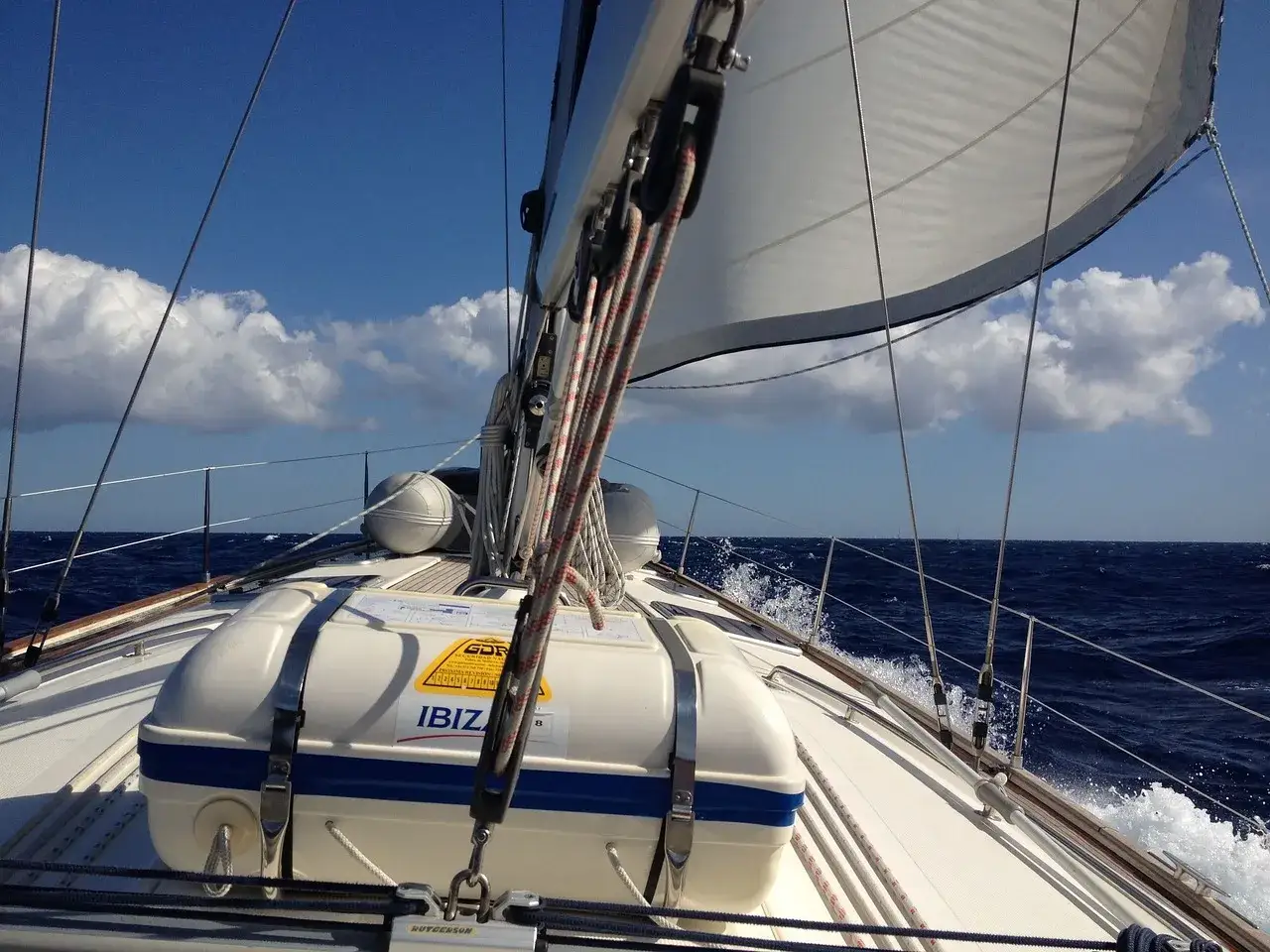 Un bateau ardent navigue sur une mer agitée sous un ciel bleu et nuageux. La voile blanche est hissée, prête pour l'aventure.