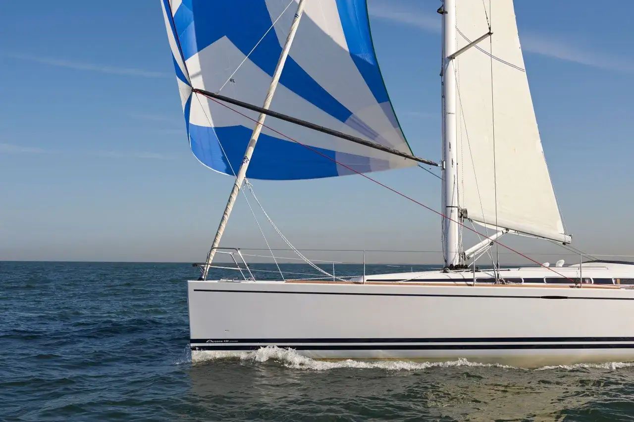Voilier blanc naviguant sur mer calme, spi symétrique bleu et blanc gonflé par le vent.