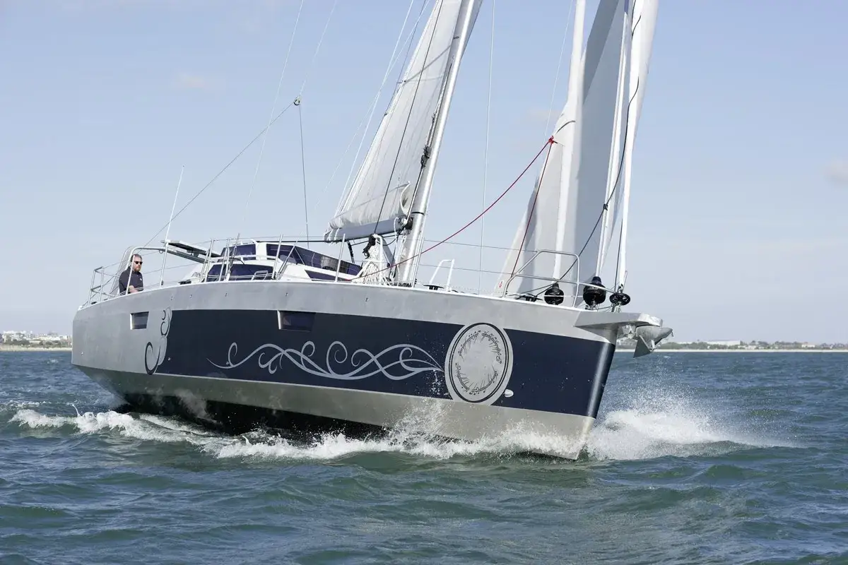 Un voilier Biloup 109 navigue sur une mer agitée, son design élégant orné de motifs stylisés.