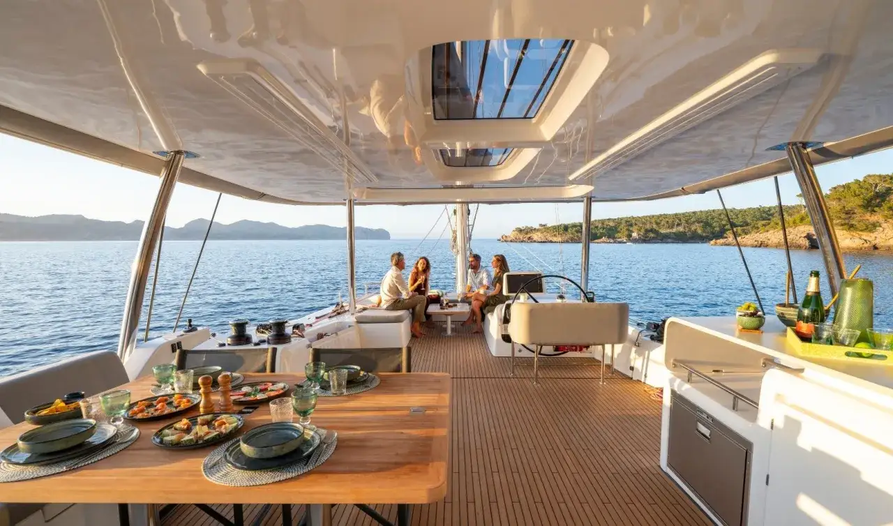 Un groupe d'amis profite d'un repas sur le pont d'un catamaran, avec une vue imprenable sur la mer et la côte. Olivier Poncin apprécie ce moment de détente.