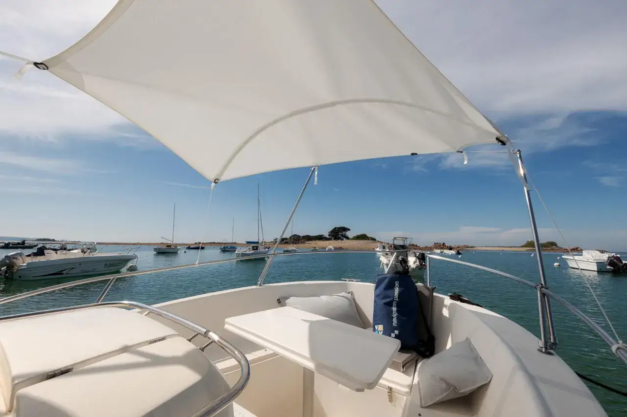 Sur un bateau, sous un taud blanc, on peut prendre un ris en admirant la mer bleue et les voiliers au mouillage.