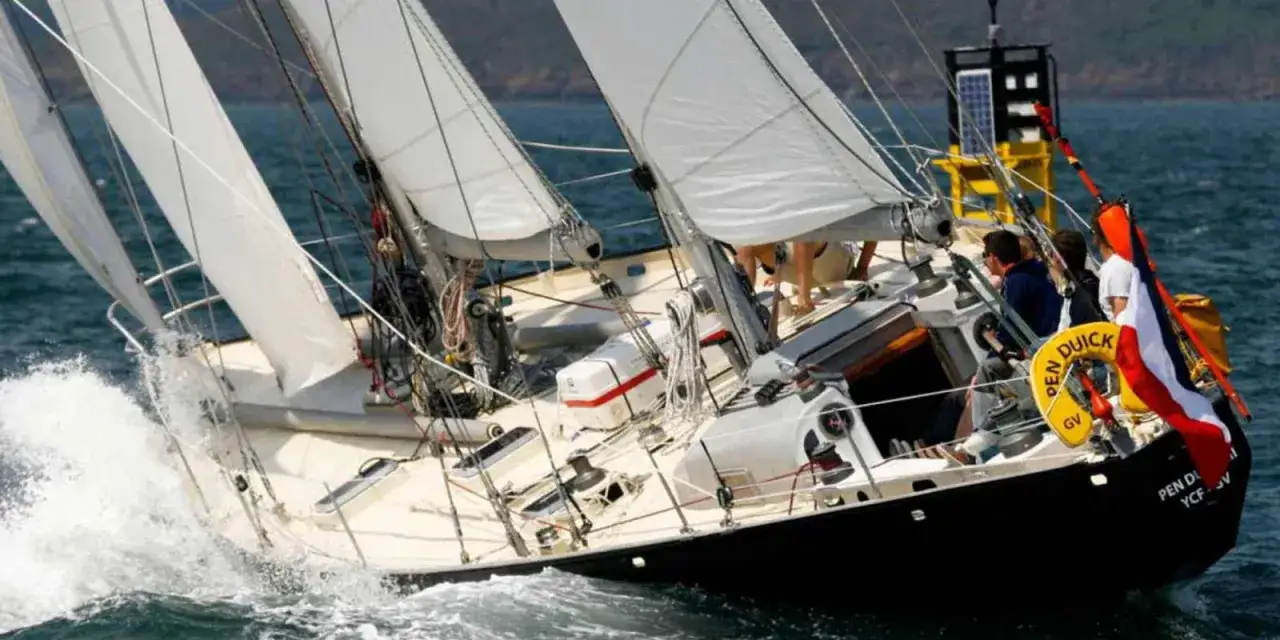Le voilier Pen Duick 3 fend les vagues, ses voiles blanches gonflées par le vent. L'équipage est concentré sur la course.