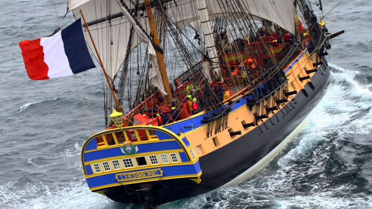 La frégate Hermione, fierté de la marine française, navigue sur une mer agitée, arborant fièrement le drapeau tricolore.