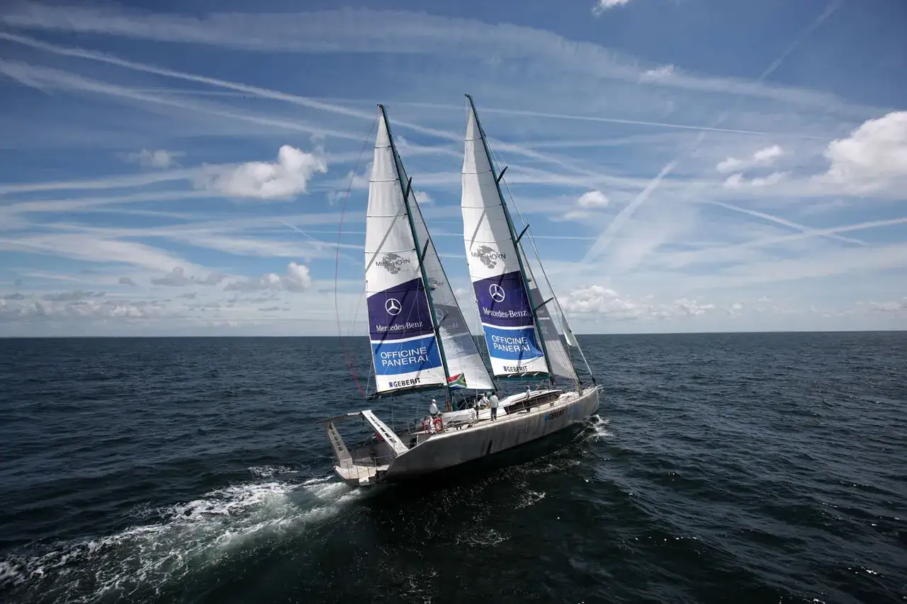 Le bateau de Mike Horn fend les vagues sous un ciel bleu parsem&eacute; de nuages et de tra&icirc;n&eacute;es de condensation.