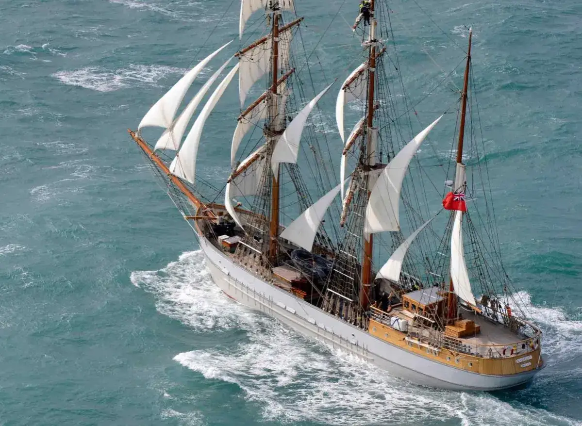 Vue a&eacute;rienne d'un navire historique aux voiles blanches gonfl&eacute;es par le vent, naviguant sur une mer agit&eacute;e. Ces grands voiliers &eacute;voquent des &eacute;poques r&eacute;volues.