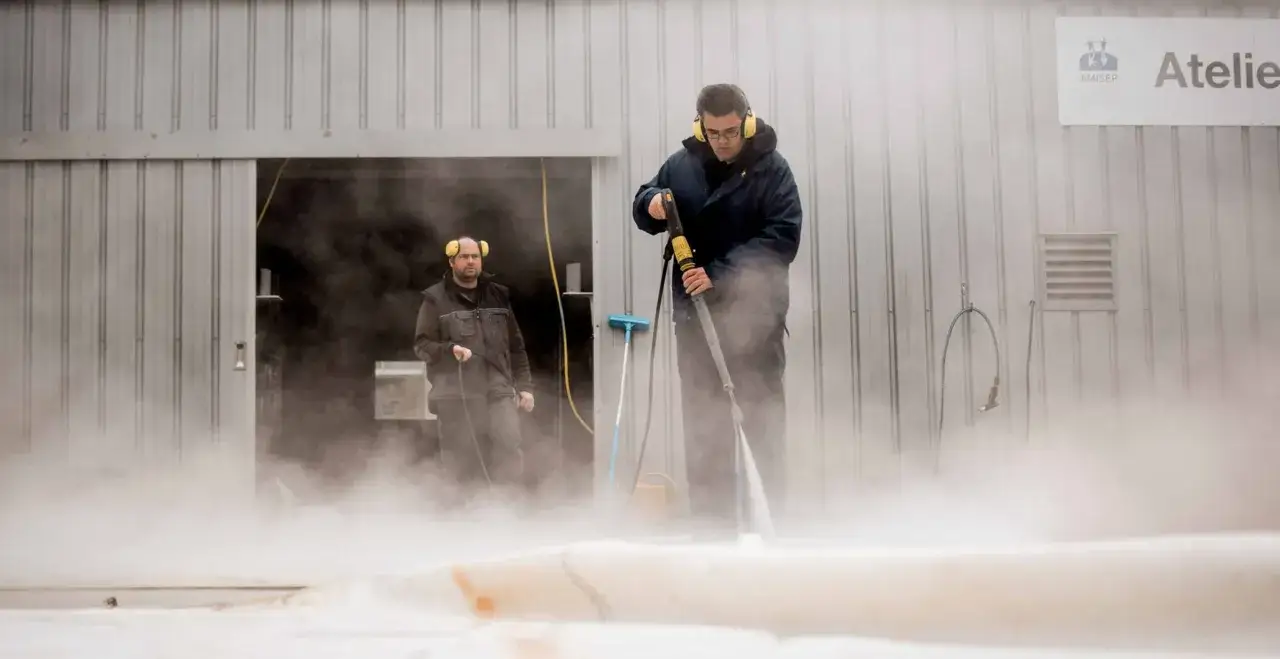 Deux hommes utilisent un nettoyeur haute pression pour nettoyer un voile de bateau avec du savon noir.