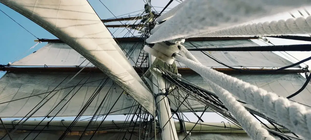Vue plongeante sur les voiles d'un voilier, cordages épais et mât. L'entretien du voilier est essentiel pour naviguer.