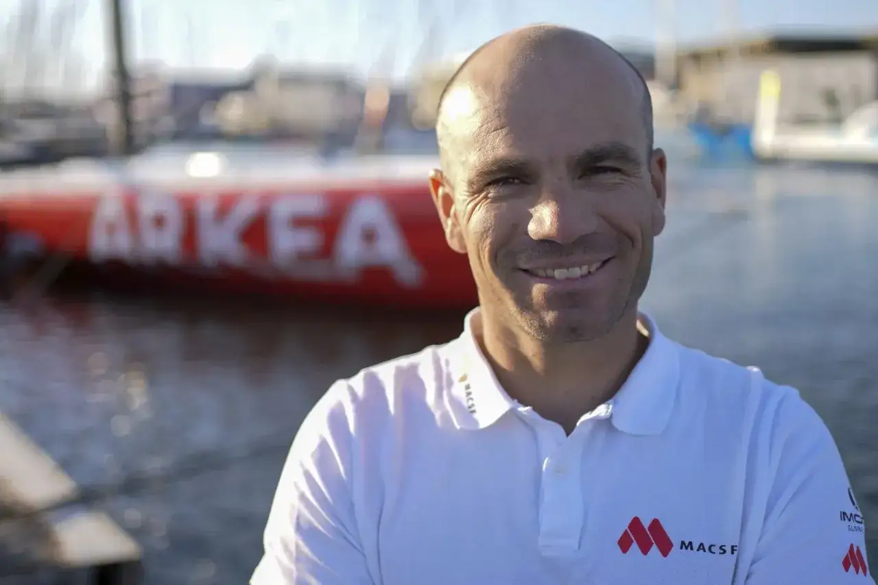Corentin Horeau, skipper souriant, pose devant un bateau de course au large marqué 