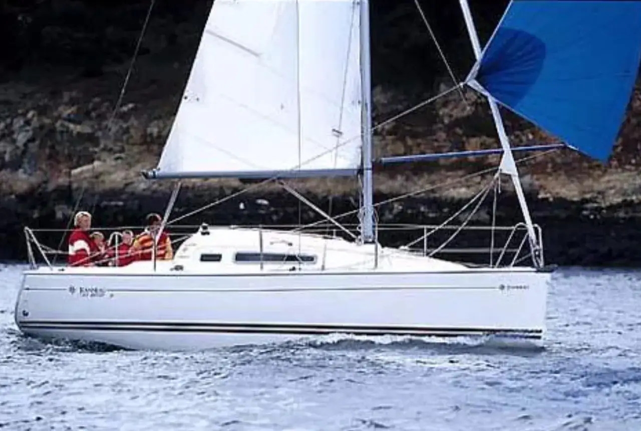 Un voilier Sun Odyssey 26 navigue sur une eau bleue, avec des personnes à bord. Les avis sur ce modèle sont positifs.