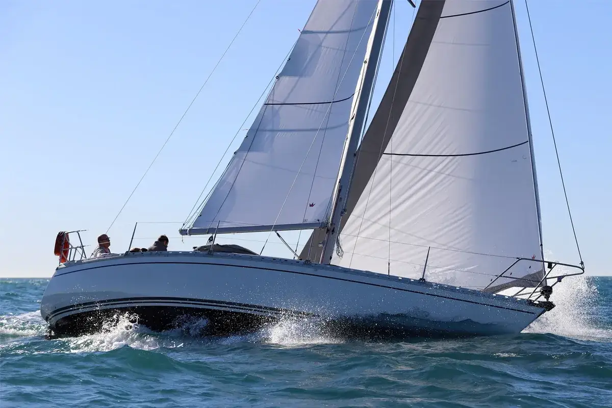 Un voilier blanc, tel un bateau symphonie, fend les vagues bleues sous un ciel clair. Deux personnes profitent de la navigation.