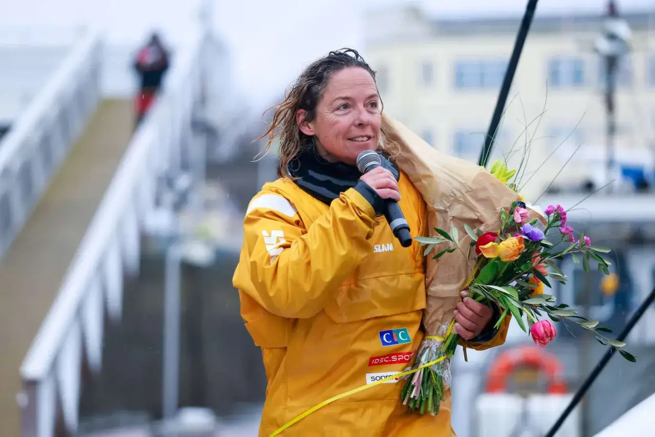 Alexia Barrier, rayonnante, reçoit un bouquet de fleurs après une course. Elle porte une veste jaune et tient un micro.