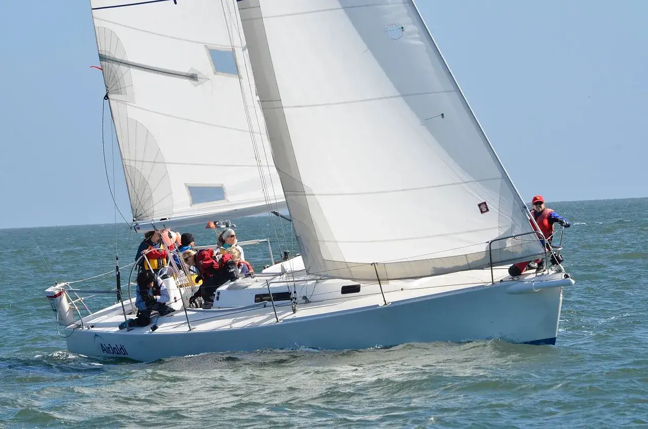 Équipage sur un voilier blanc naviguant sur une mer agitée. Le giter du bateau est léger, les voiles sont gonflées par le vent.