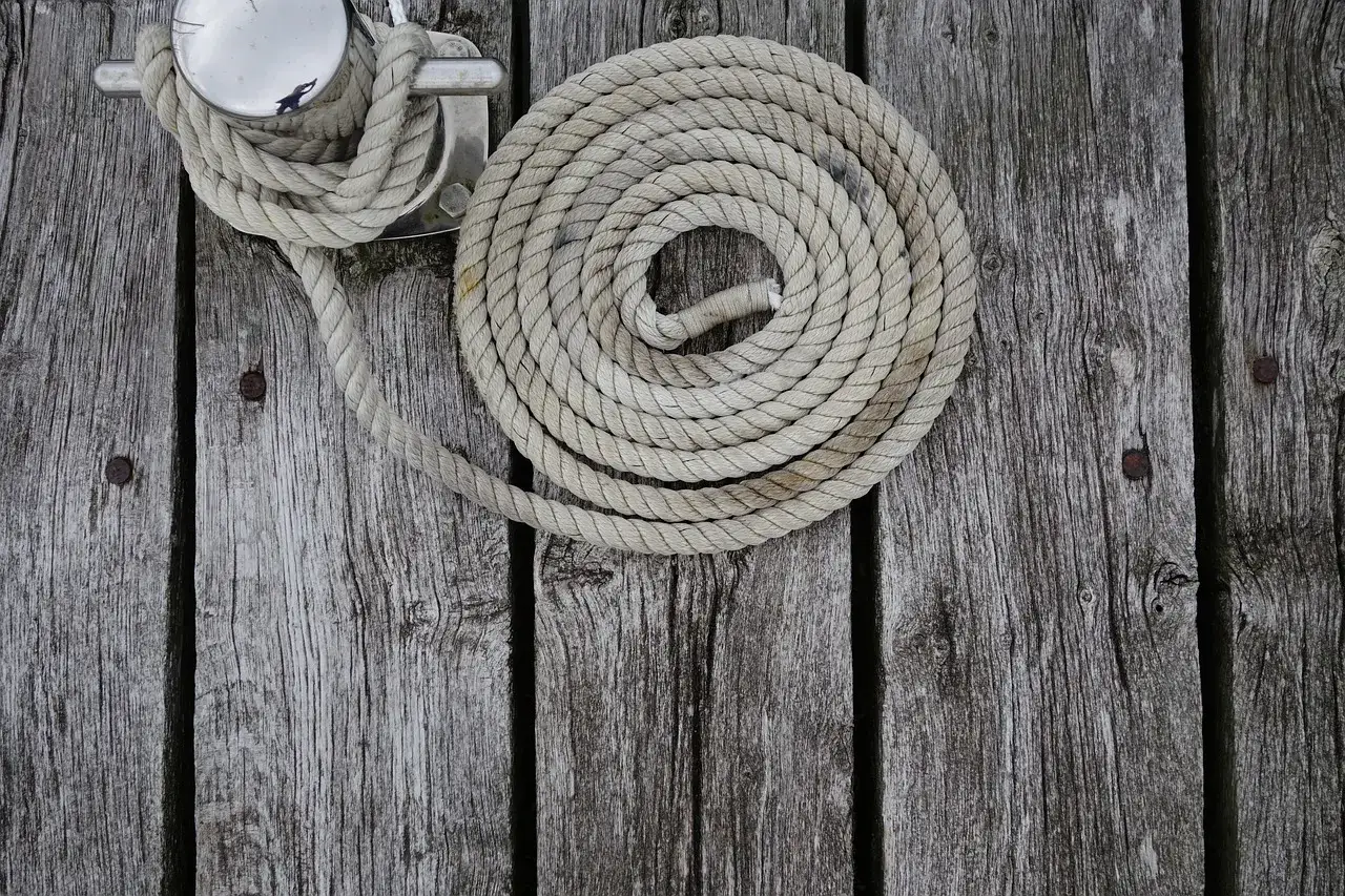 Corde enroulée en spirale sur un tableau de bois vieilli, attachée à une bitte d'amarrage. Un nœud marin facile pour sécuriser le bateau.