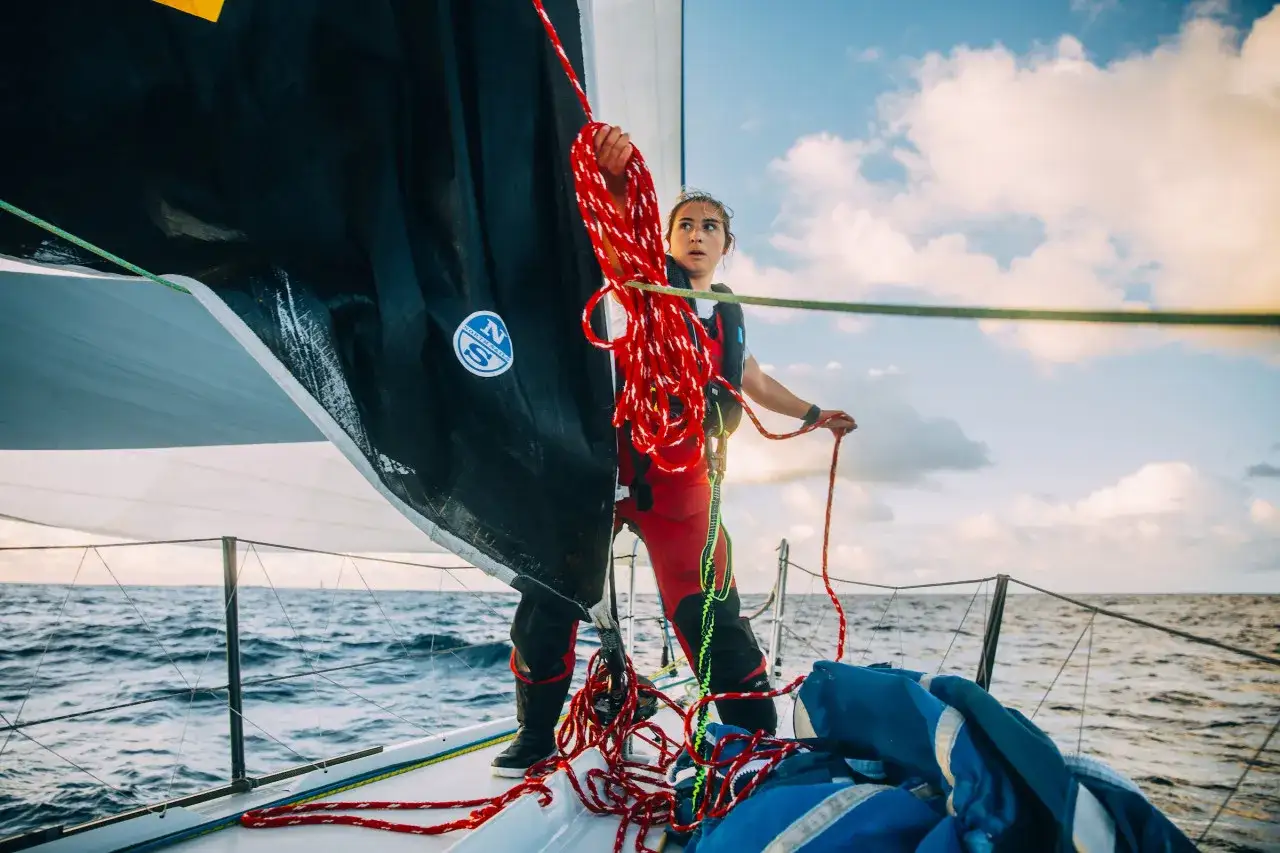 Sébastien Destremau, concentré, manœuvre les cordages d'un voilier en pleine mer, sous un ciel nuageux.