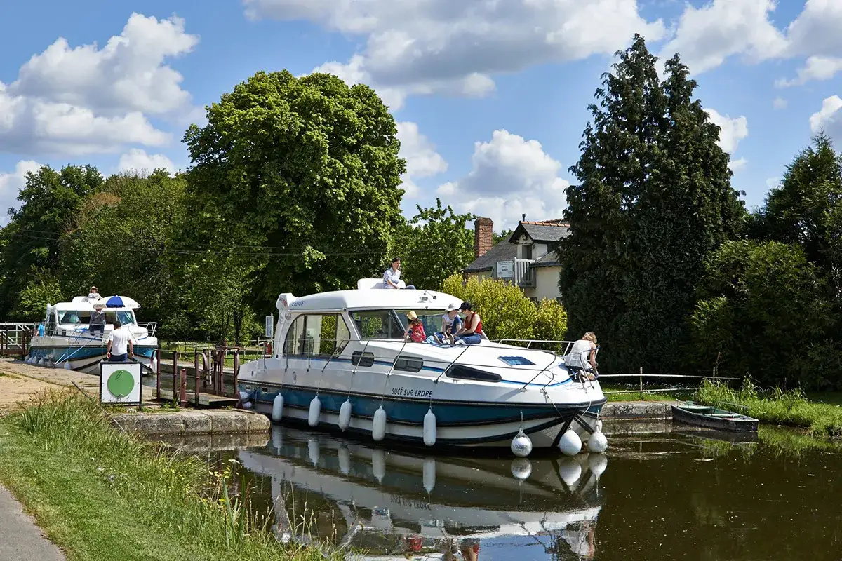Une famille profite d'une belle journée pour remonter la vilaine en bateau, naviguant paisiblement sur le canal bordé d'arbres verdoyants.