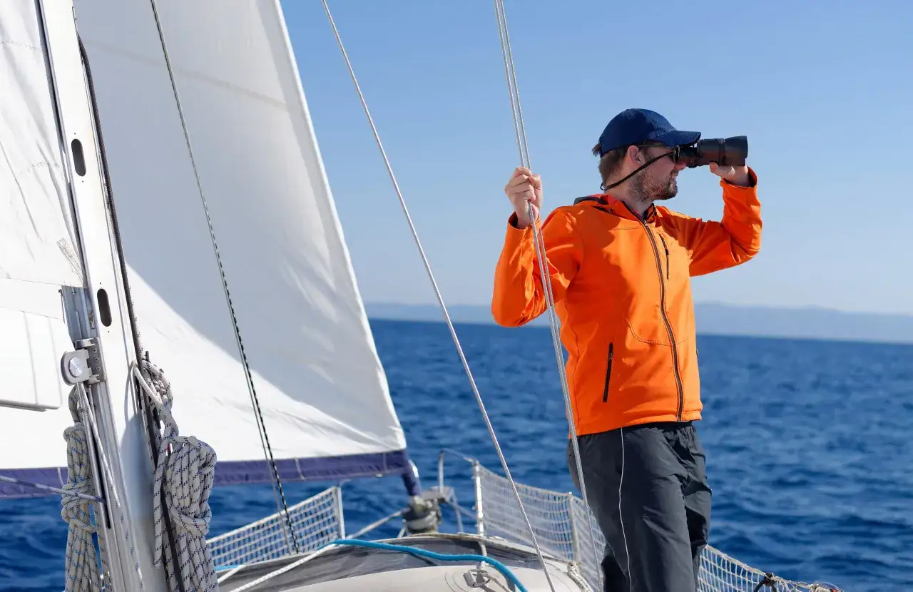 Un homme en voilier utilise des jumelles pour observer l'horizon. Un guide pour comment choisir des jumelles.