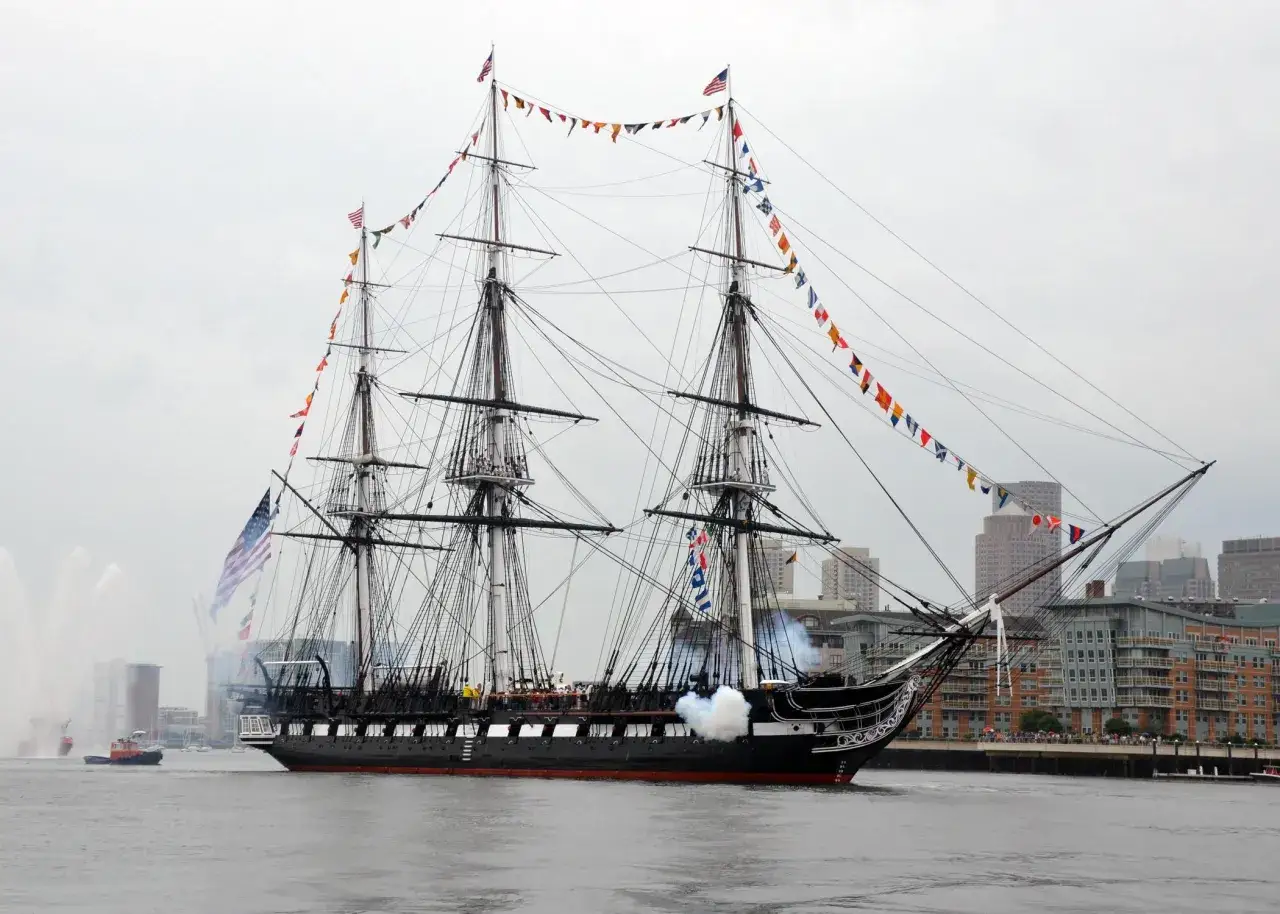 Le majestueux shtandart bateau, orn&eacute; de drapeaux color&eacute;s, navigue fi&egrave;rement sur l'eau, salu&eacute; par des canons fumants.
