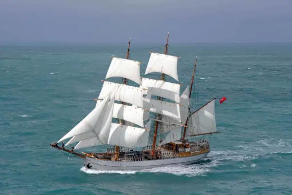 Majestueux voilier 3 mats, ses voiles blanches gonflées par le vent, navigue sur une mer agitée.