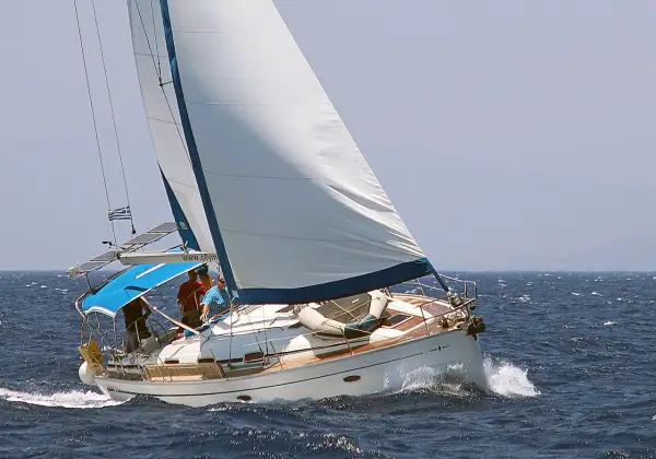 Un voilier blanc navigue sur une mer bleue agitée. L'équipage semble prendre un ris, ajustant les voiles pour mieux affronter le vent.